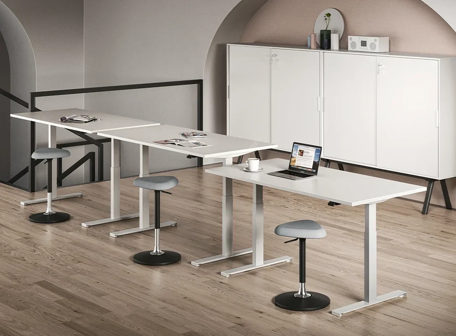 Λευκά γραφεία ρυθμιζόμενου ύψους σε μοντέρνο επαγγελματικό χώρο με σκαμπό και ντουλάπια.